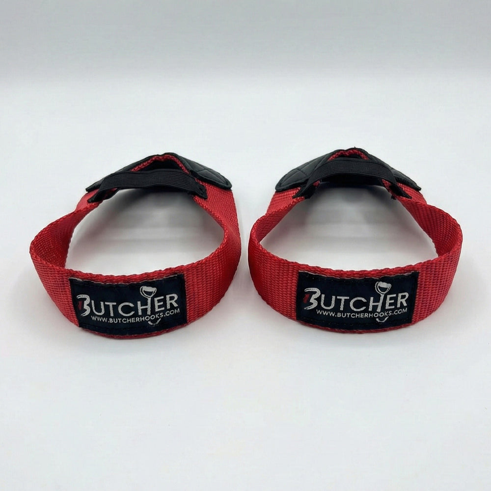 Pair of red Butcher Hooks weightlifting straps with black rubber hooks and stitched Butcher branding, designed for improved grip and support during heavy lifting.