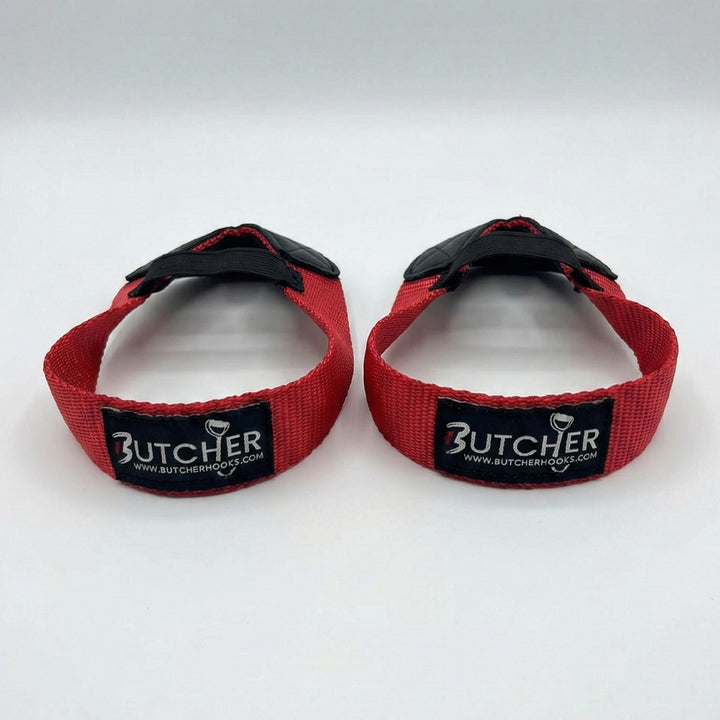 Pair of red Butcher Hooks weightlifting straps with black rubber hooks and stitched Butcher branding, designed for improved grip and support during heavy lifting.